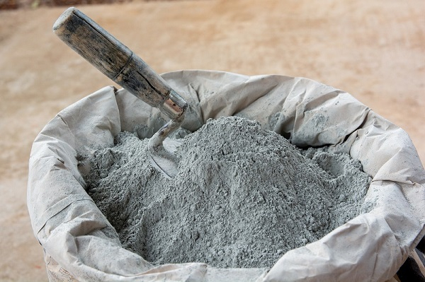 11611821 | Ghanaguardian.com Bag of gray cement powder with a wooden trowel resting on top, ready for mixing on a construction site.
