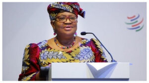 African woman in colorful traditional dress speaking at a podium with a microphone, delivering a speech at a formal event.