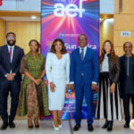 Eight professionals in formal attire pose for a group photo at a conference, with an AEF banner in the background.