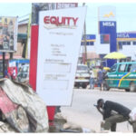 Street scene with a tall Equity signboard center, billboards, and parked vans in the background.