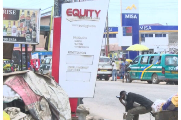 Street scene with a tall Equity signboard center, billboards, and parked vans in the background.