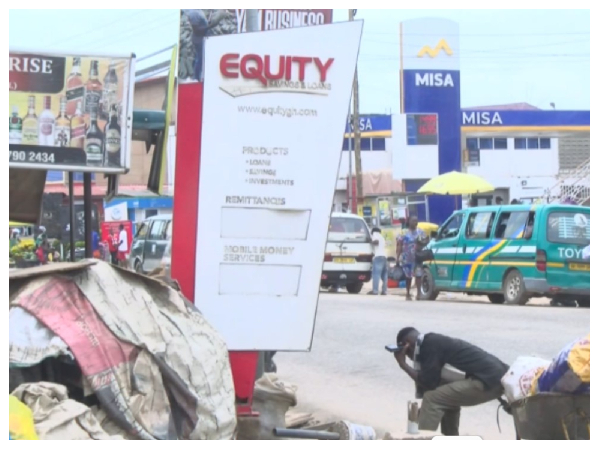 Street scene with a tall Equity signboard center, billboards, and parked vans in the background.