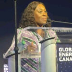 Woman speaking at a clear podium during the Global Energy Show Canada, wearing a striped purple and green blouse.
