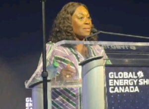 Woman speaking at a clear podium during the Global Energy Show Canada, wearing a striped purple and green blouse.