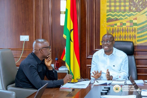 Two men in a formal meeting at a wooden conference table, with flags behind them and Ministry of Energy and Green Transition branding visible.