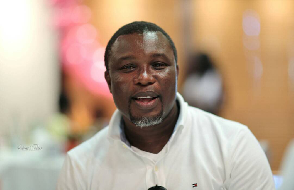 31538590 | Ghanaguardian.com Portrait of a smiling man in a white polo shirt at an indoor event, sunglasses tucked into his shirt.