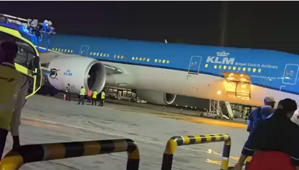 KLM Royal Dutch Airlines plane on the tarmac at night with ground crew preparing cargo and passengers near the jet engine area.