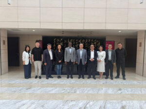 Twelve professionals in business attire pose for a group photo on marble steps outside a building with a black plaque featuring gold calligraphy.