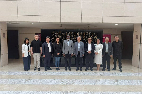 Twelve professionals in business attire pose for a group photo on marble steps outside a building with a black plaque featuring gold calligraphy.