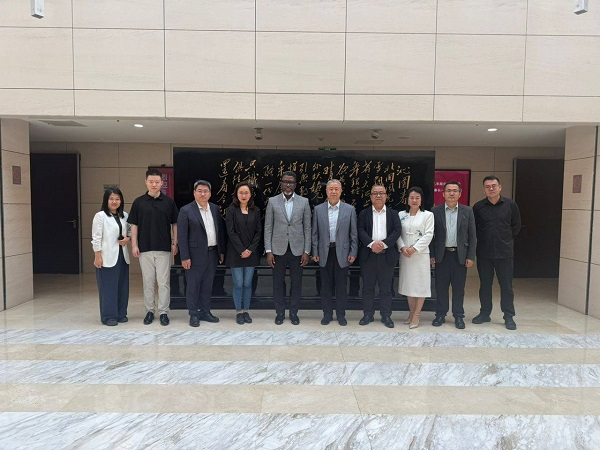 Twelve professionals in business attire pose for a group photo on marble steps outside a building with a black plaque featuring gold calligraphy.
