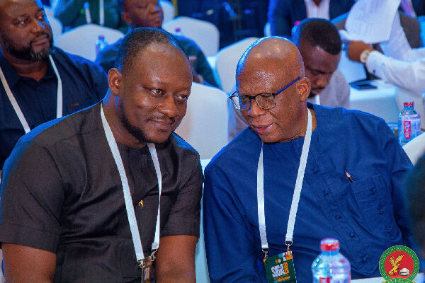 48497049 | Ghanaguardian.com Two men wearing lanyards sit side by side at a conference, one in a black shirt and the other in blue, conversing.