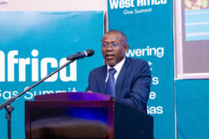 Man in a dark blue suit delivering a speech at a podium during a gas summit, with blue banners in the background.