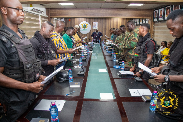 Group of uniformed security officers standing around a long conference table, reviewing documents in a formal meeting.