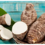 Taro roots with sliced pieces on a green leaf in a wicker basket against a turquoise wooden background.