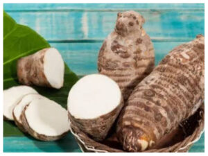 Taro roots with sliced pieces on a green leaf in a wicker basket against a turquoise wooden background.
