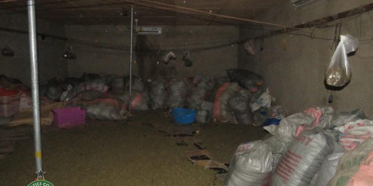 Dim basement storage area with many large bags stacked along the walls, a blue bucket, and miscellaneous clutter under low lighting.