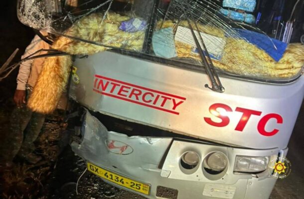 Front of a gray Intercity bus with a severely cracked windshield and scattered debris after a collision, nighttime scene.