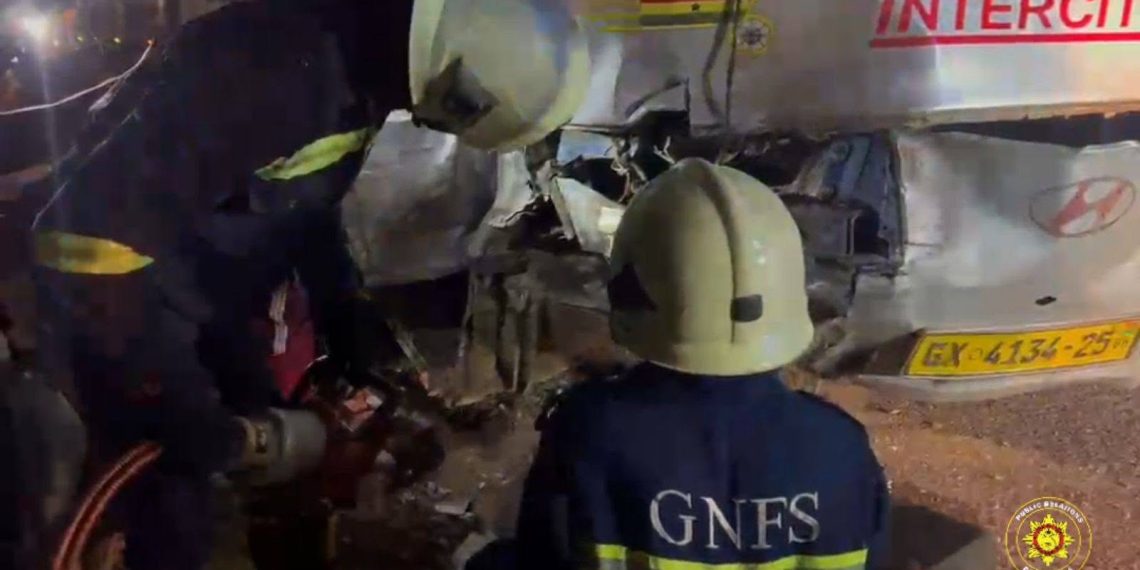 Nighttime scene of firefighters and responders in helmets inspecting a severely damaged truck after a crash, debris scattered nearby.