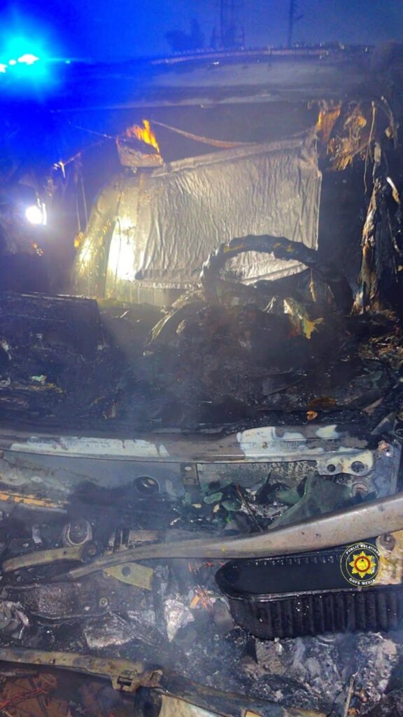 Burnt car interior with charred debris and a blue emergency light in the background, indicating a recent fire scene.