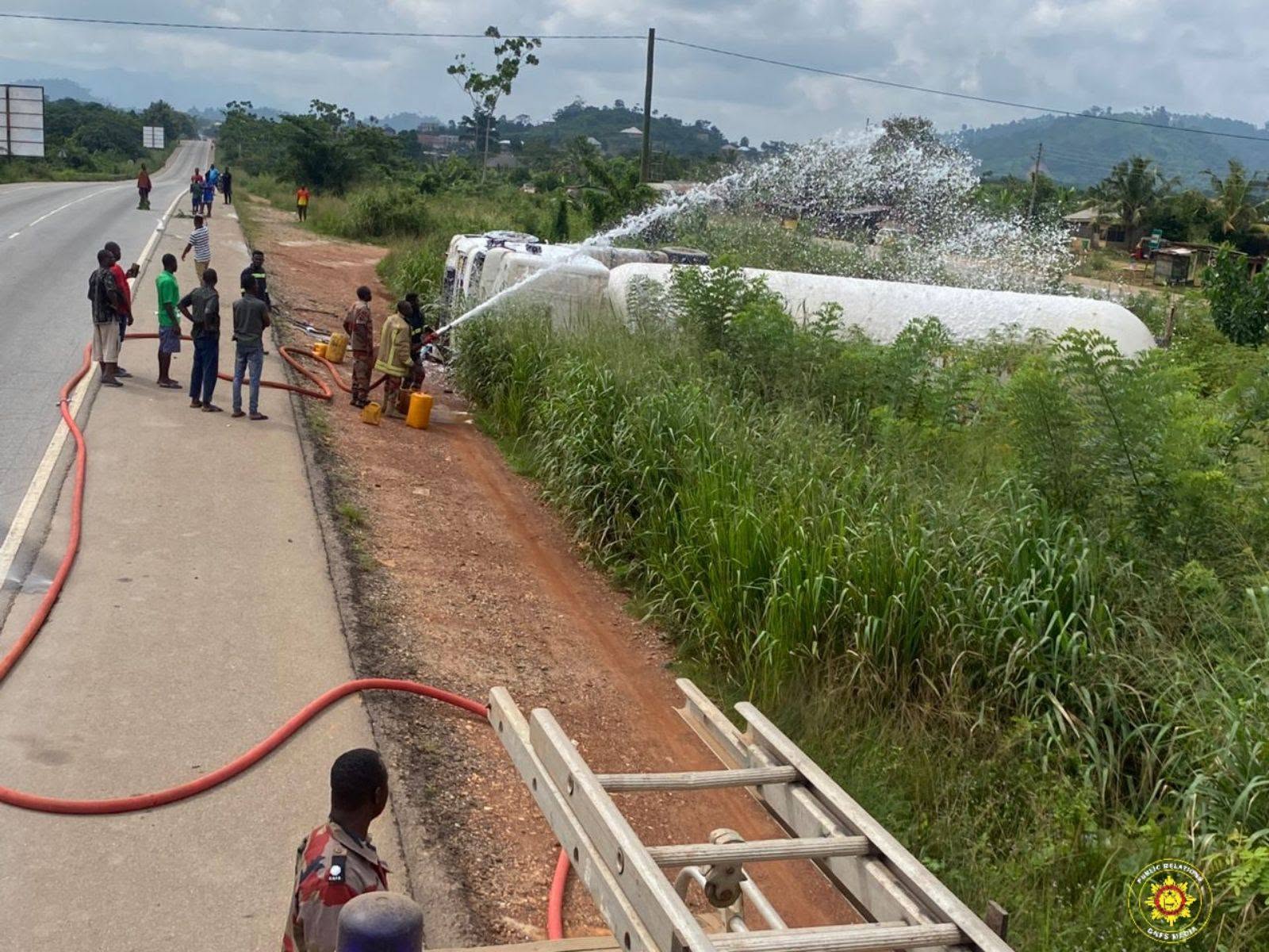 719864917_1018456897359930_2668607725677333572_n | Ghanaguardian.com Firefighters spray a large hose toward a white tanker on a grassy roadside while bystanders watch along a rural highway.