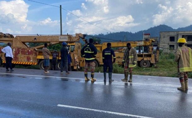 722306062_1018456854026601_6244298433007430892_n-750x375 | Ghanaguardian.com People in work clothes and firefighters stand on a wet highway beside a large yellow crane truck; hills and a building under construction are in the background.