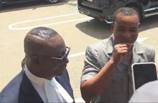 ANDY-APPIAH-KUBI2 | Ghanaguardian.com Two men stand in a parking lot; one in a dark suit and sunglasses, the other in a light gray jacket, gesturing as a smartphone is held up.