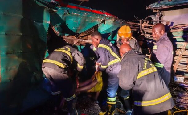 Accident | Ghanaguardian.com Nighttime rescue operation: firefighters and volunteers carry a person away from a crushed bus amid debris on a dark scene.