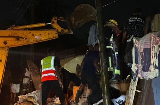 Nighttime rescue scene with workers clearing rubble from a collapsed building; a yellow crane arm visible in the left foreground.