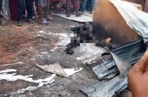 A crowd of bystanders watches a charred, damaged object on the street; debris and ash are scattered on the ground, with a pixelated figure suggesting a person harmed in the incident.