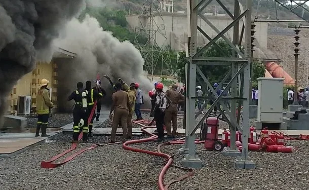 Firefighters battle a blaze with hoses as thick black smoke billows from a building area.