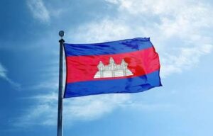 Cambodian national flag waving on a flagpole with Angkor Wat centerpiece against a blue sky.