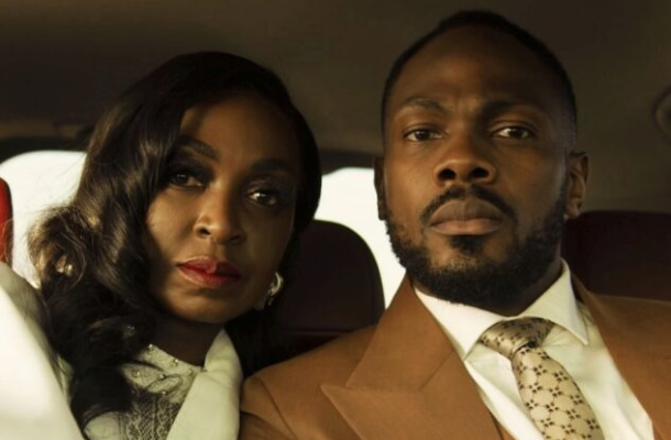 A man and woman sit close together in a car, looking at the camera.