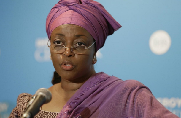 Woman wearing a purple head wrap and glasses speaks into a microphone at a press event.