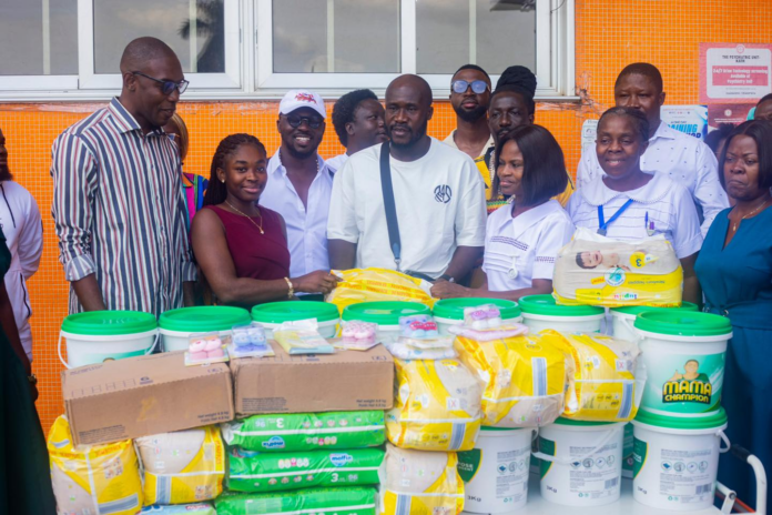 Group of diverse volunteers posing with donated supplies (diapers, buckets) outside an orange tiled wall.