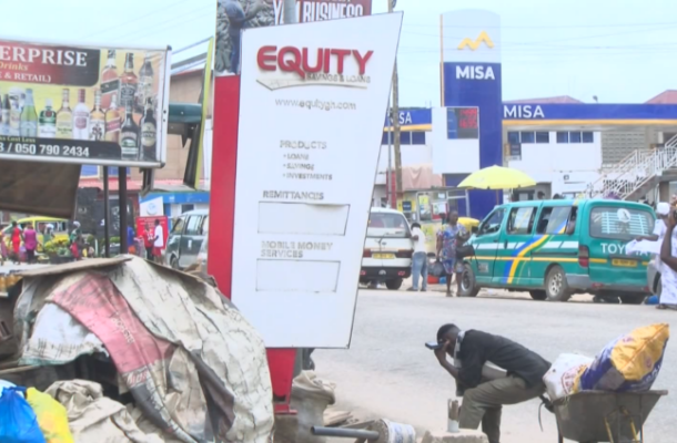 Equity-Savings-and-Loans | Ghanaguardian.com Street scene with an Equity sign advertising loans and savings; market stalls and a green-blue minivan in the background.