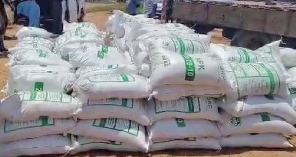 Fertilizer | Ghanaguardian.com Stacks of white sacks with green labels piled on the ground beside a truck, likely construction materials.