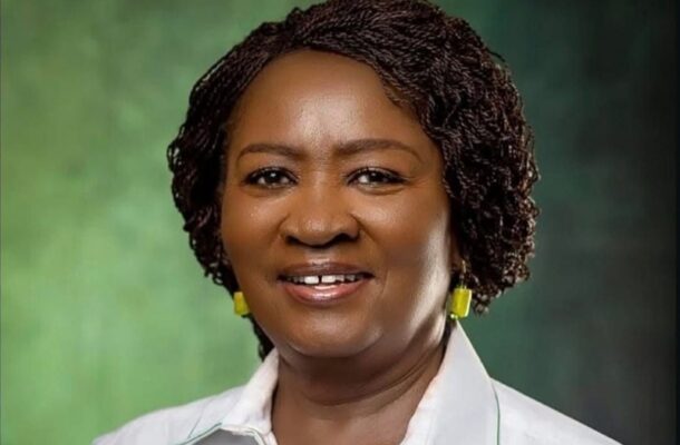 Portrait of a smiling Black woman with short braided hair, wearing a white collared shirt and yellow earrings, against a green studio backdrop.