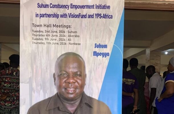 Banner for Suhum Constituency Empowerment Initiative with Town Hall Meeting dates; a man stands in front of the sign poster.