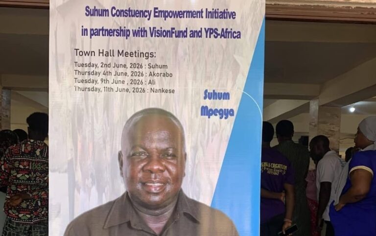 Banner for Suhum Constituency Empowerment Initiative with Town Hall Meeting dates; a man stands in front of the sign poster.