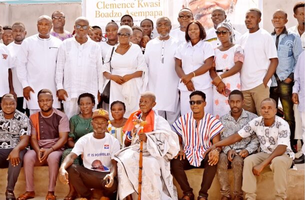 Group of men and women posing on steps, many wearing white outfits, with an elderly man holding a staff at the center image shows a crowd.