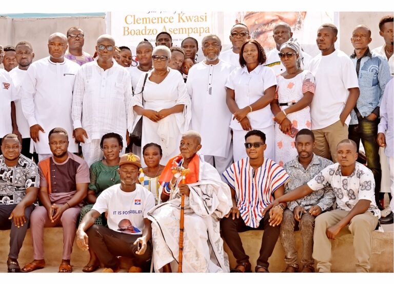 Group of men and women posing on steps, many wearing white outfits, with an elderly man holding a staff at the center image shows a crowd.