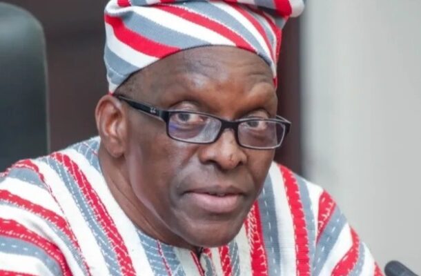 Man wearing a red, white, and gray striped traditional outfit with a matching headwrap and glasses, looking at the camera.
