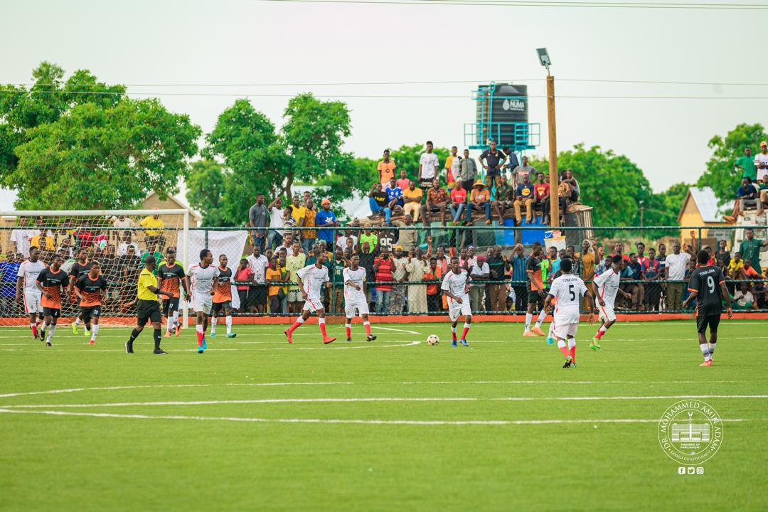 IMG-20260608-WA0008 | Ghanaguardian.com Soccer match on a green field with players in white and black uniforms and a crowd watching behind a fence.