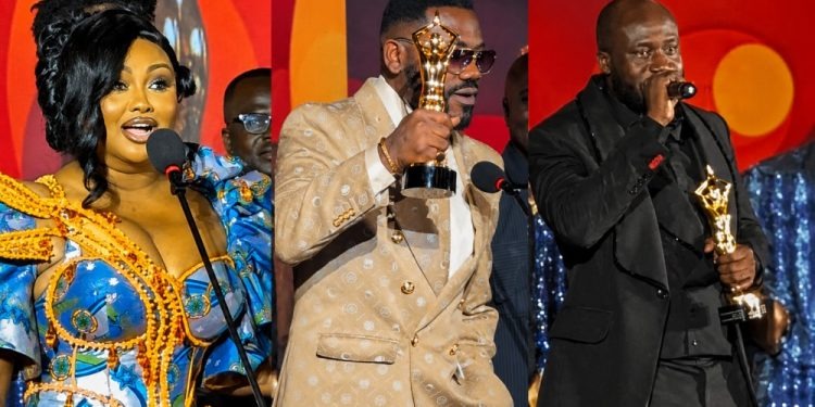 Three award winners stand on a stage, each holding a trophy and speaking into microphones during an ceremonies moment.