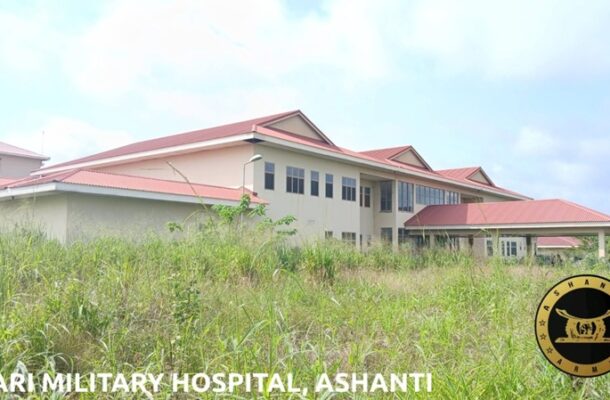 IMG-20260610-WA0021-1-1536x863 | Ghanaguardian.com Exterior of Afari Military Hospital in Ashanti: beige building with red roof, set behind tall grass, with a circular emblem on the right.