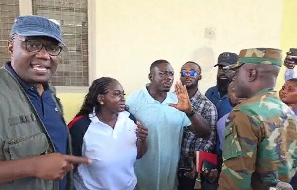 IMG-20260610-WA0023 | Ghanaguardian.com Group of civilians speaking to a soldier in camouflage; a man in a light blue shirt raises his hand as others look on outside a building with a pale wall.