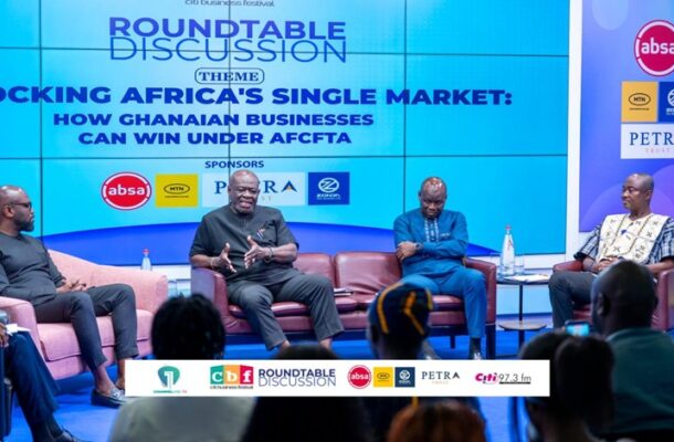 Panel discussion on stage: four men seated on pink chairs beneath a large blue screen reading 'Roundtable Discussion' and 'Locking Africa's Single Market: How Ghanaian Businesses Can Win Under AfCFTA' with sponsor logos nearby.