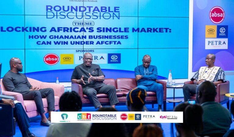 Panel discussion on stage: four men seated on pink chairs beneath a large blue screen reading 'Roundtable Discussion' and 'Locking Africa's Single Market: How Ghanaian Businesses Can Win Under AfCFTA' with sponsor logos nearby.