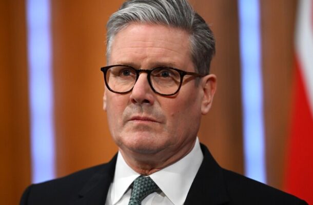 Portrait of a middle-aged man with gray hair and black-framed glasses, wearing a dark suit and green tie.
