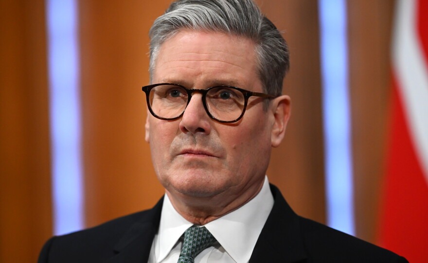 Portrait of a middle-aged man with gray hair and black-framed glasses, wearing a dark suit and green tie.